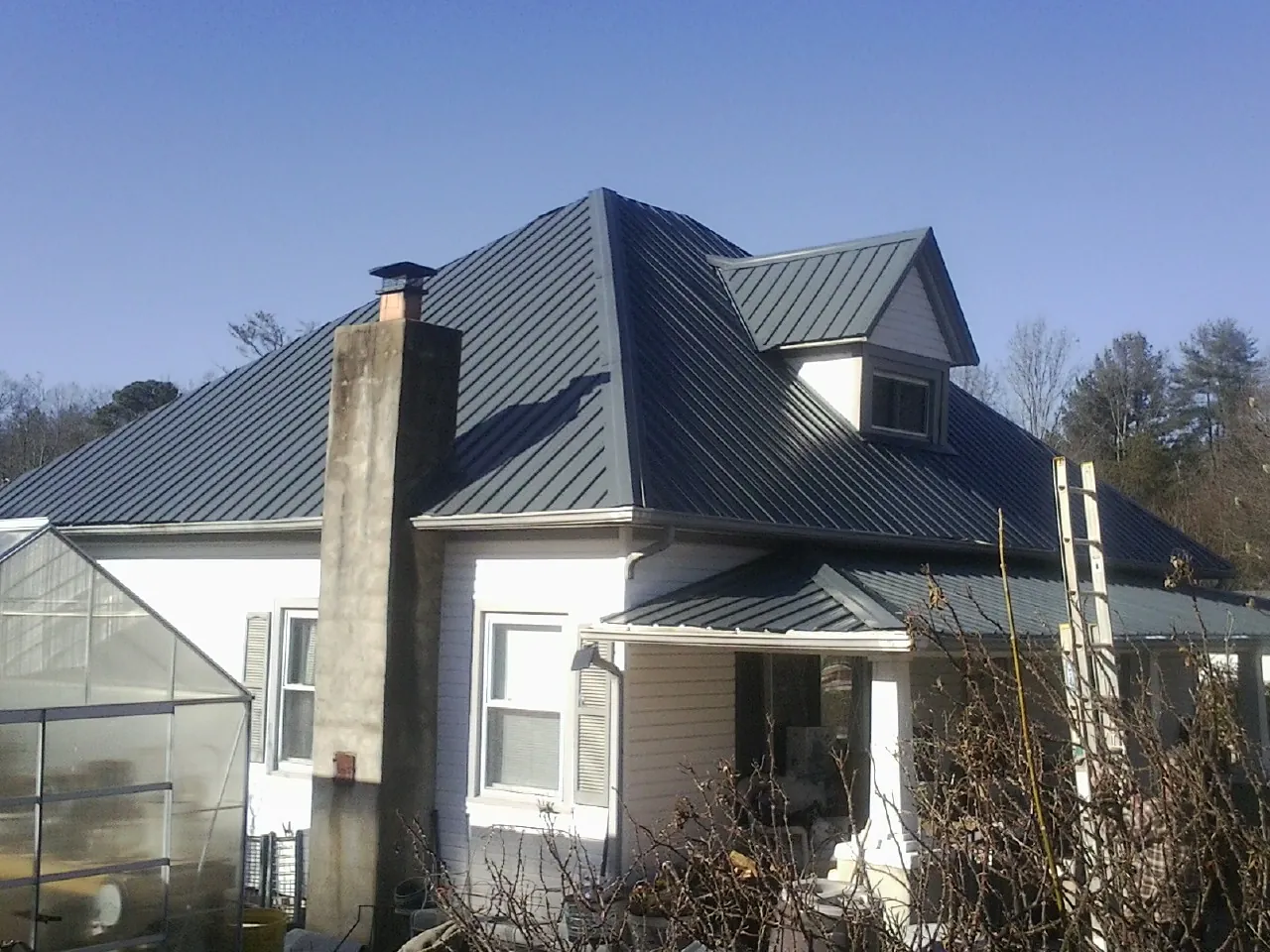 Dark blue standing seam metal roof on a white farmhouse with dormer — Slate & Tile Roof Repair by Roofing Brothers in Stout