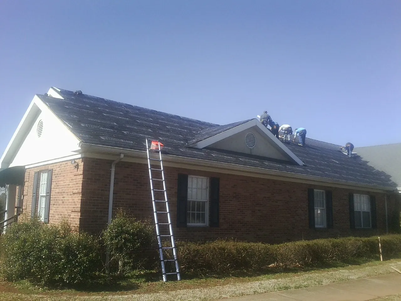 Crew tearing shingles off a brick ranch roof with a ladder set — Emergency Roof Repair work by our crew in Stout