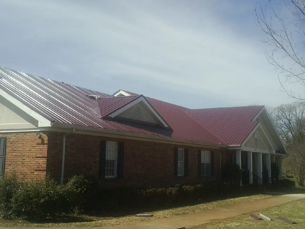 Red metal roof with gabled entries on a long brick building, from a Hail Damage Roof Repair job in Stout