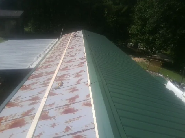 Old rusted panels beside newly installed green metal roofing — Wind Damage Roof Repair by Roofing Brothers in Stout