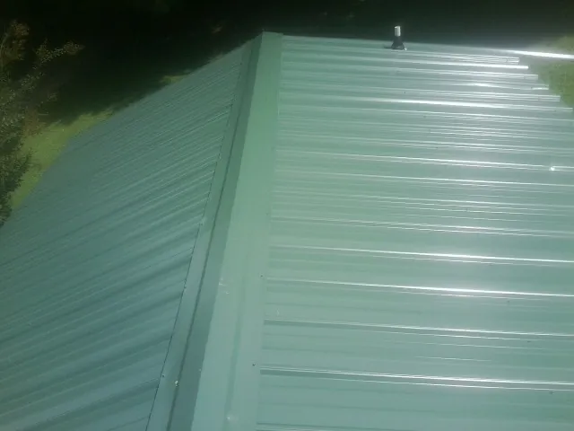 New green metal panels meeting at the ridge of a roof — Flat Roof Repair work by our crew in Stout