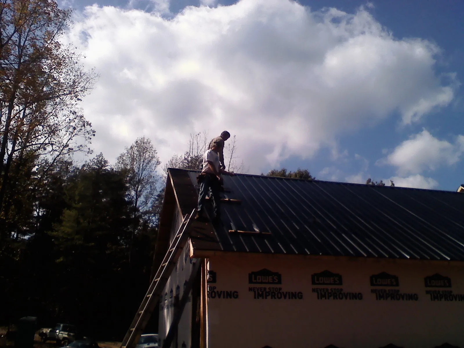 Roofer fastening dark metal panels high against a cloudy sky, from a Roof Inspection job in Stout