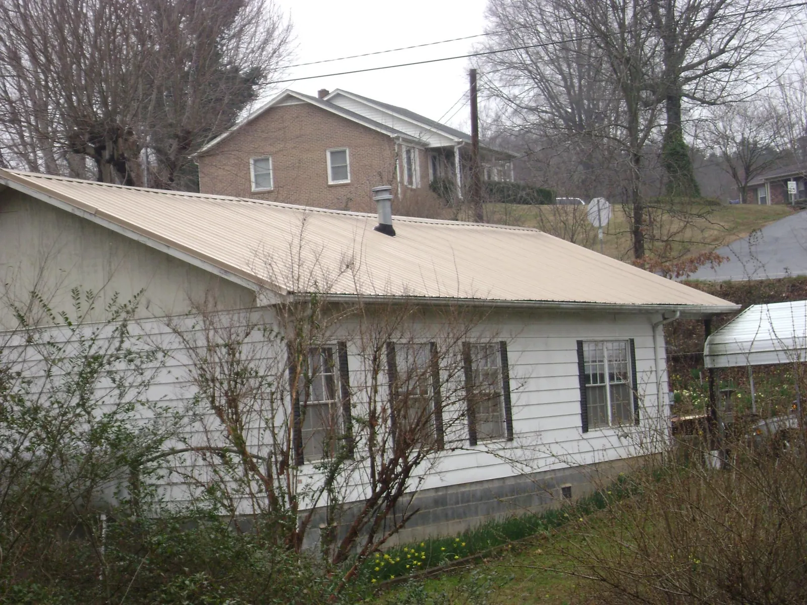 Tan metal roof on a white sided house set into a hillside — Commercial Roofing by Roofing Brothers in Stout