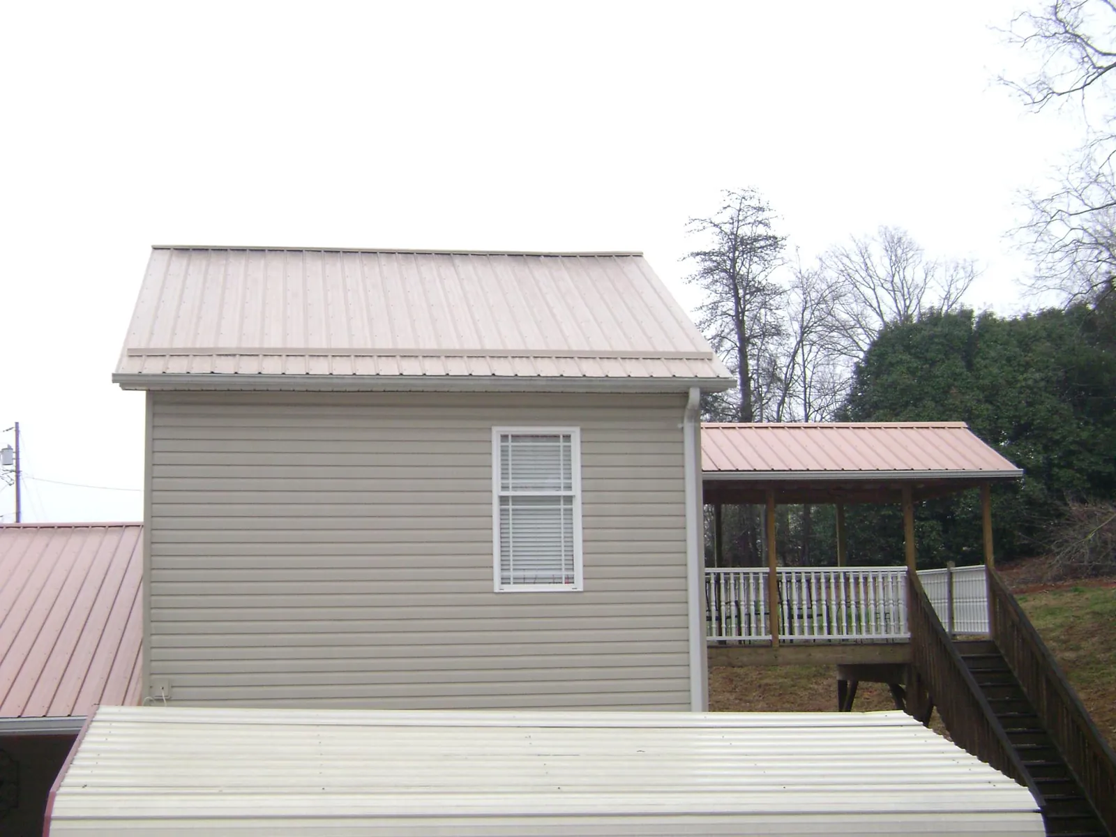 Tan metal roofs on a two story addition and attached porch, from a Roof Replacement job in Stout